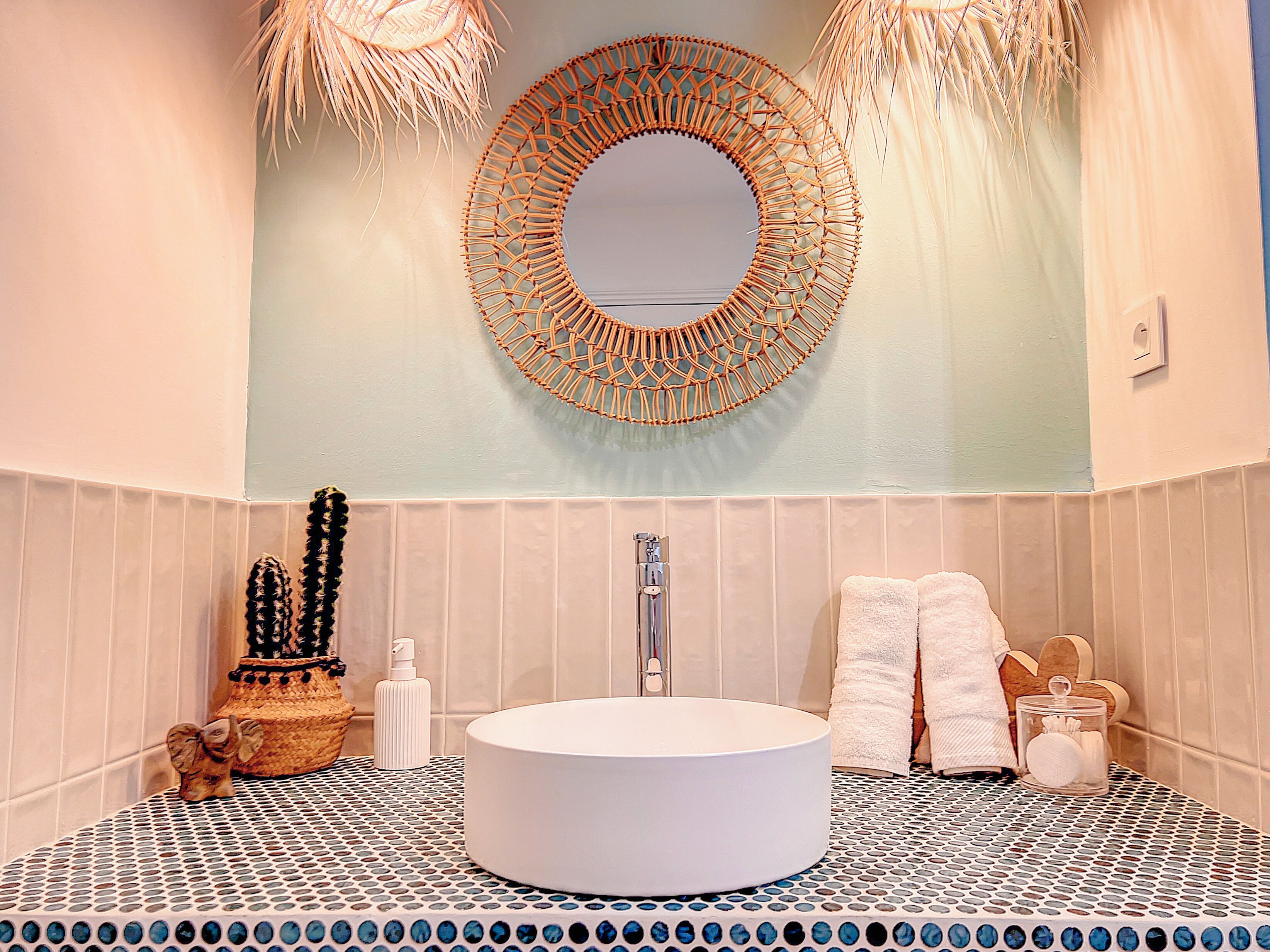 Une salle de bain avec un lavabo rond blanc, un miroir à motifs tissés et un carrelage décoré.