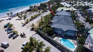 An aerial view of a resort with a large building, a swimming pool, and a beach area with palm trees and parked cars. - Princess Manon, Beachfront, Feet in water,  Ocean view, Pool (Saint-Martin)