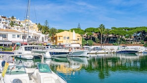 A marina with various boats docked, a building with a yellow facade, and a row of white buildings with balconies.