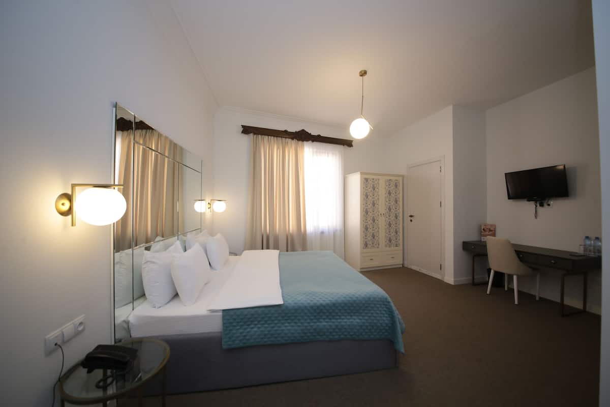 A hotel room with a bed, bedside table, desk, chair, TV, and wardrobe.