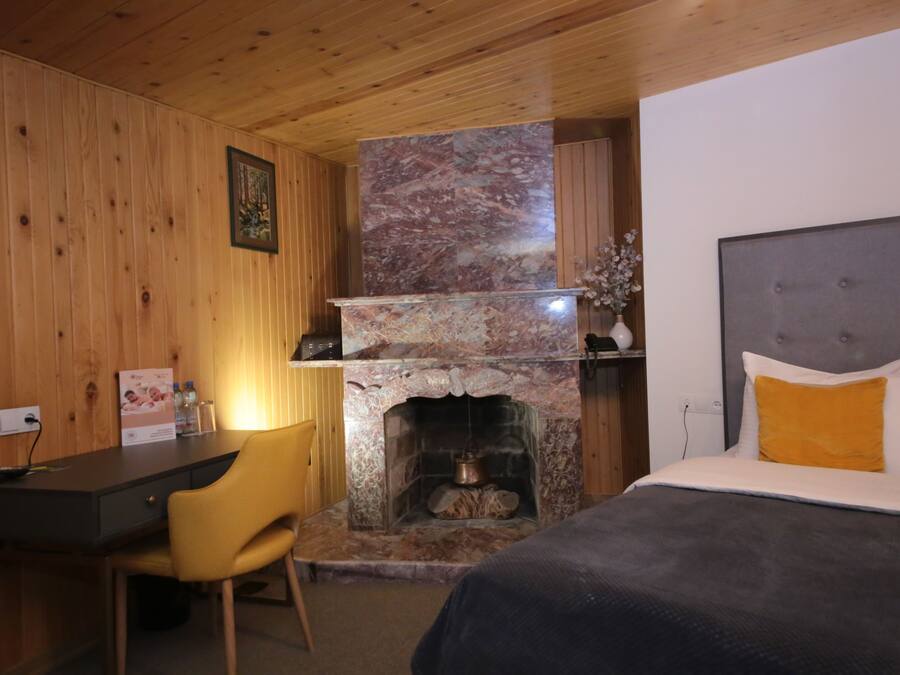 Una habitación con cama, escritorio, sillón, chimenea y paredes de madera.