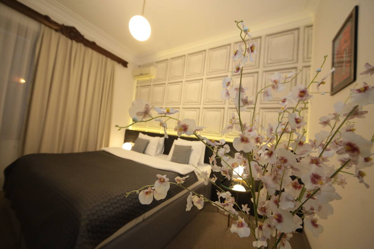 A hotel room with a bed, a vase of white orchids, and a white paneled wall.