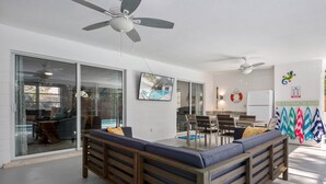 Un soggiorno moderno con vista piscina, porte scorrevoli in vetro, ventilatori a soffitto e un'area pranzo anch'essa con vista sulla piscina.