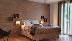 A bedroom with a bed, bedside lamps, a chair, and a view of greenery through the window. - Charming Provencal villa in the heart of the forest and  the village of Lorgues (Lorgues)