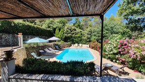 A pool area with lounge chairs, umbrellas, and a stone wall. - Charming Provencal villa in the heart of the forest and  the village of Lorgues (Lorgues)