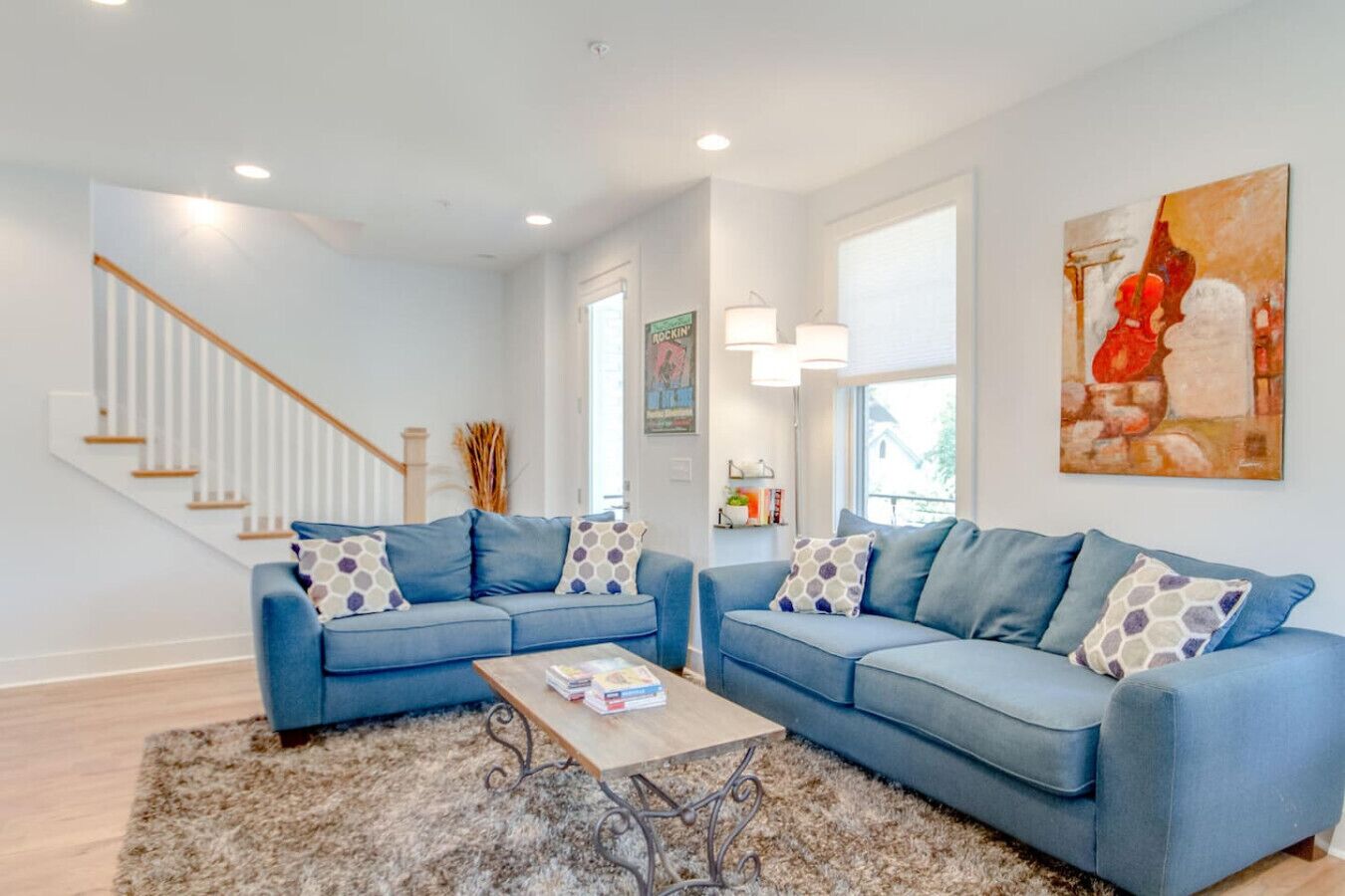 A modern living room with two blue sofas, a coffee table, and a staircase.