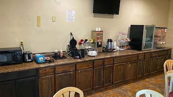 A breakfast bar with a microwave, toaster, waffle maker, and coffee maker. There are chairs and a table in the foreground.