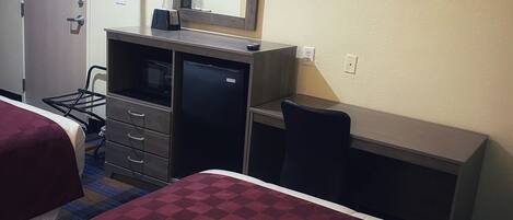 A hotel room with two beds, a desk, a dresser, a mirror, a TV, and a coat rack.