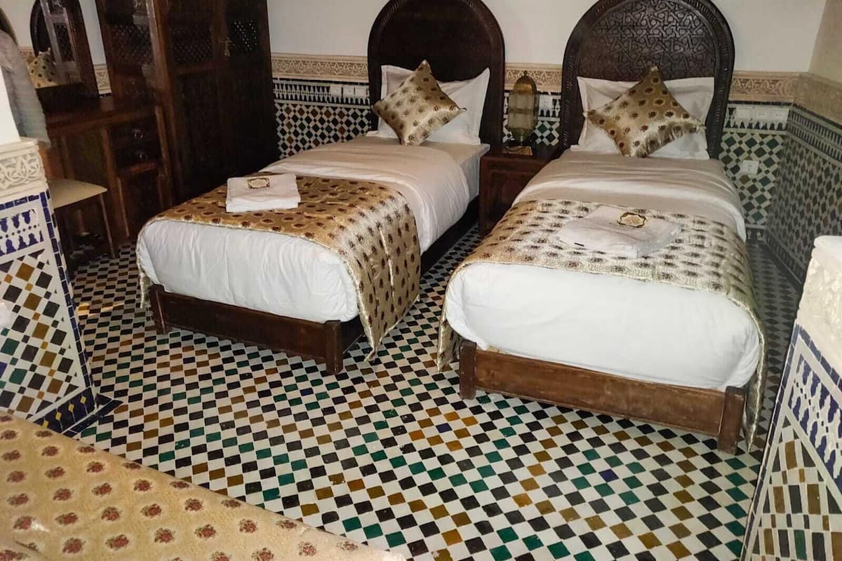 Quarto de hotel com duas camas, piso de azulejos xadrez e um detalhe decorativo na parede.