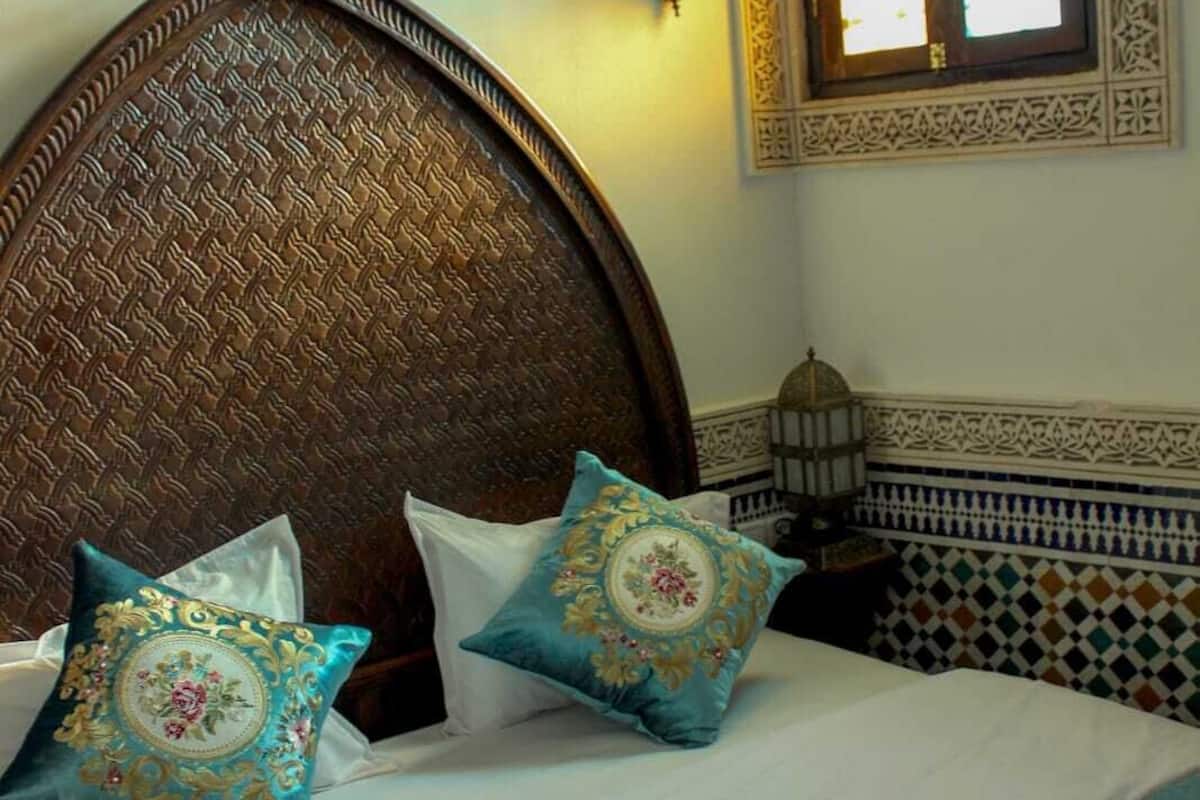 Cama com cabeceira de madeira, duas almofadas decorativas e colcha estampada.