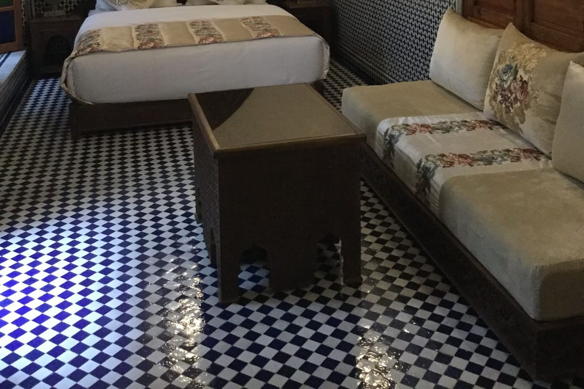 Quarto com cama, sofá, mesa pequena, paredes com padrão e iluminação decorativa.