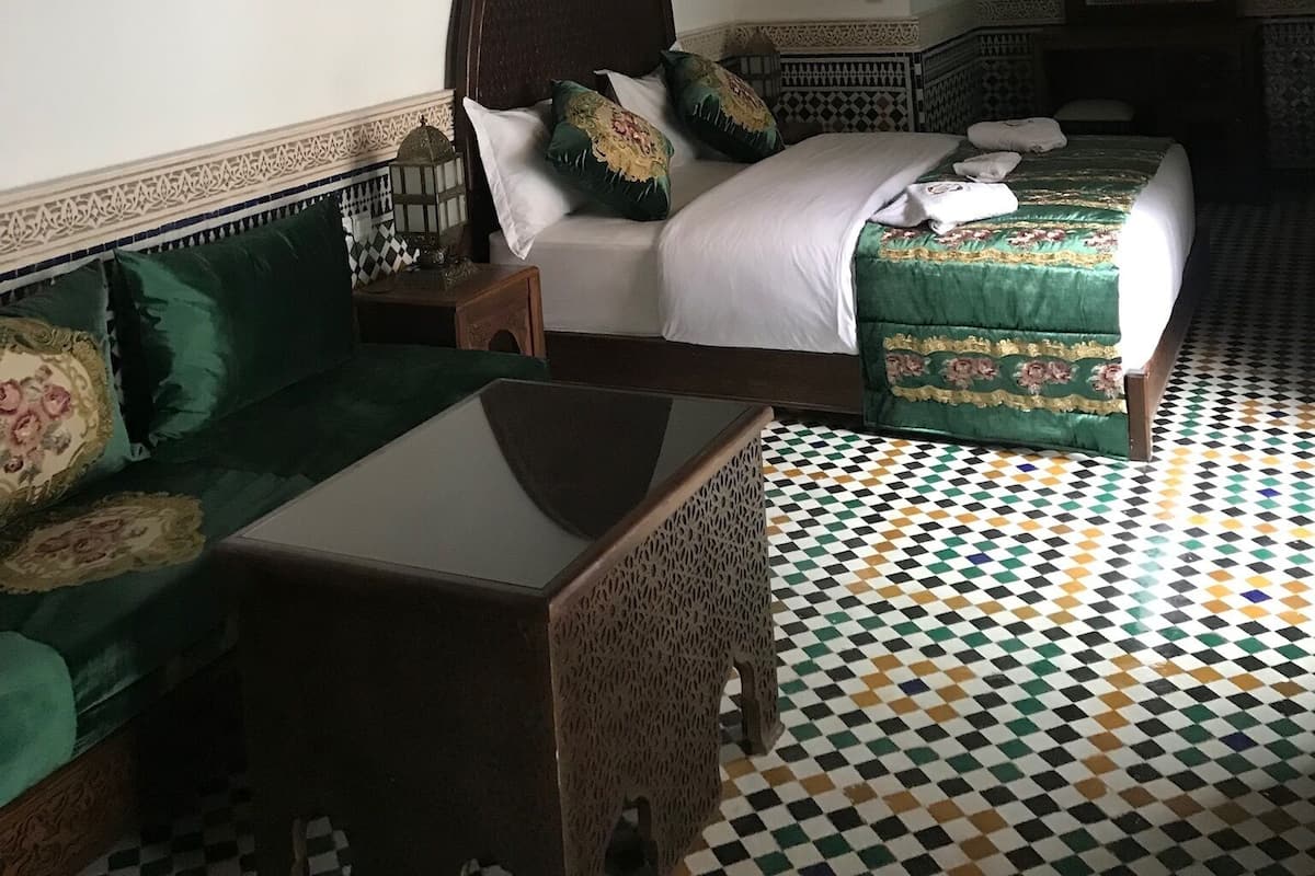 Quarto com cama, sofá, mesa e piso estampado.