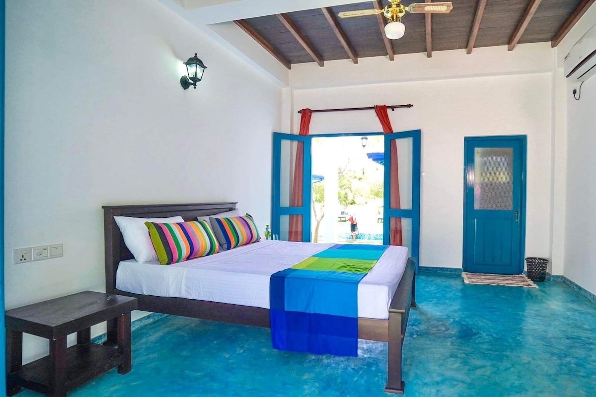 A bedroom with a bed, a bench, a wardrobe, and a view of the outside.