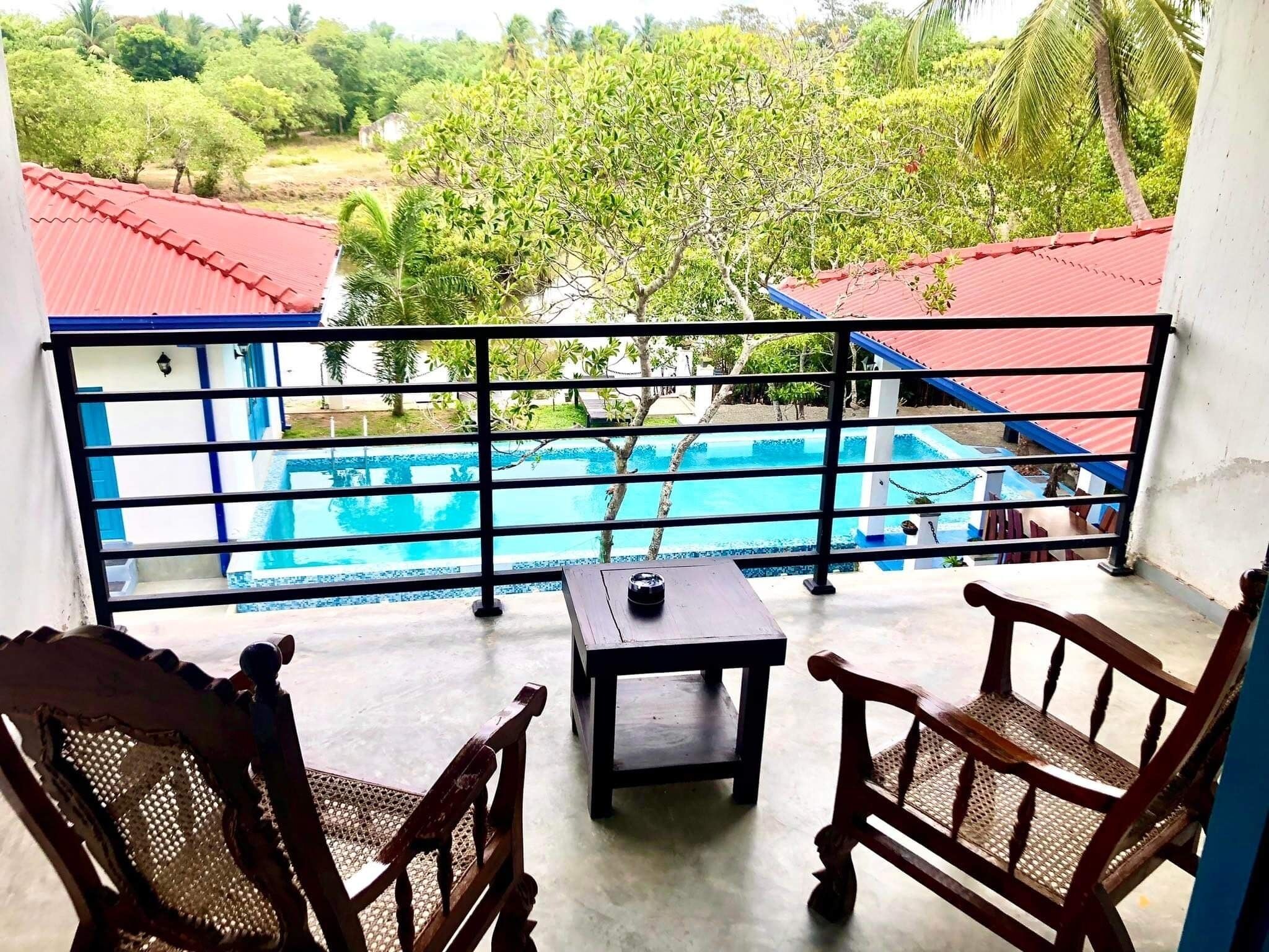 Un balcón con vista a una piscina, rodeado de follaje y palmeras.