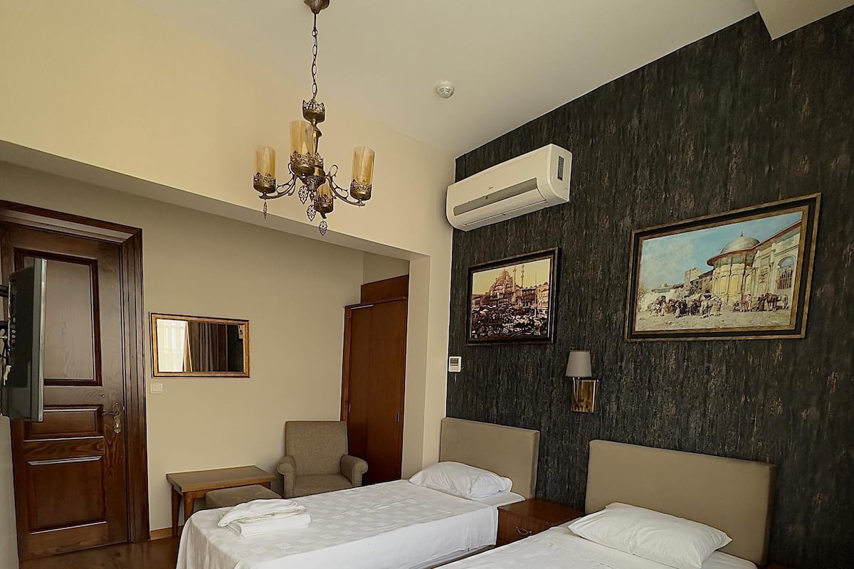 Une chambre d’hôtel avec deux lits, un plancher en bois, un lustre, un climatiseur et deux tableaux au mur.