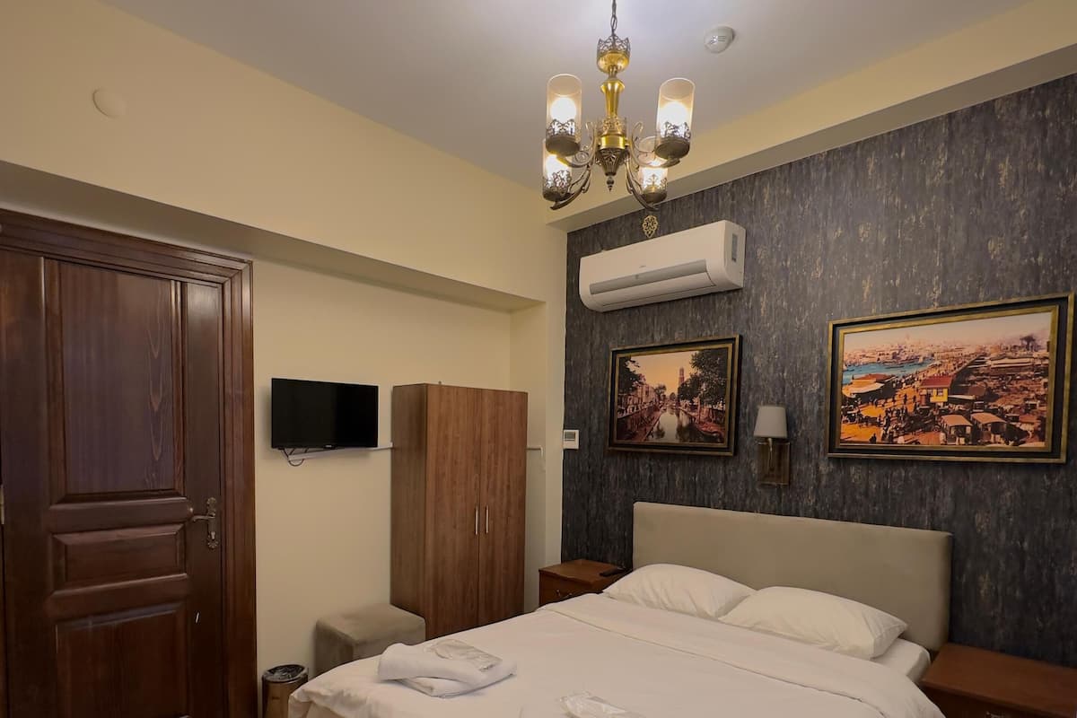 Une chambre d’hôtel avec un grand lit, une armoire en bois, un téléviseur à écran plat, un lustre et deux tableaux accrochés au mur.