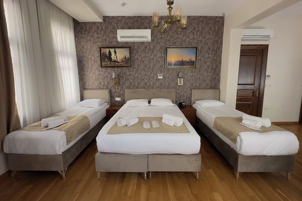 Une chambre d’hôtel avec trois lits, un lustre et deux tableaux au mur.