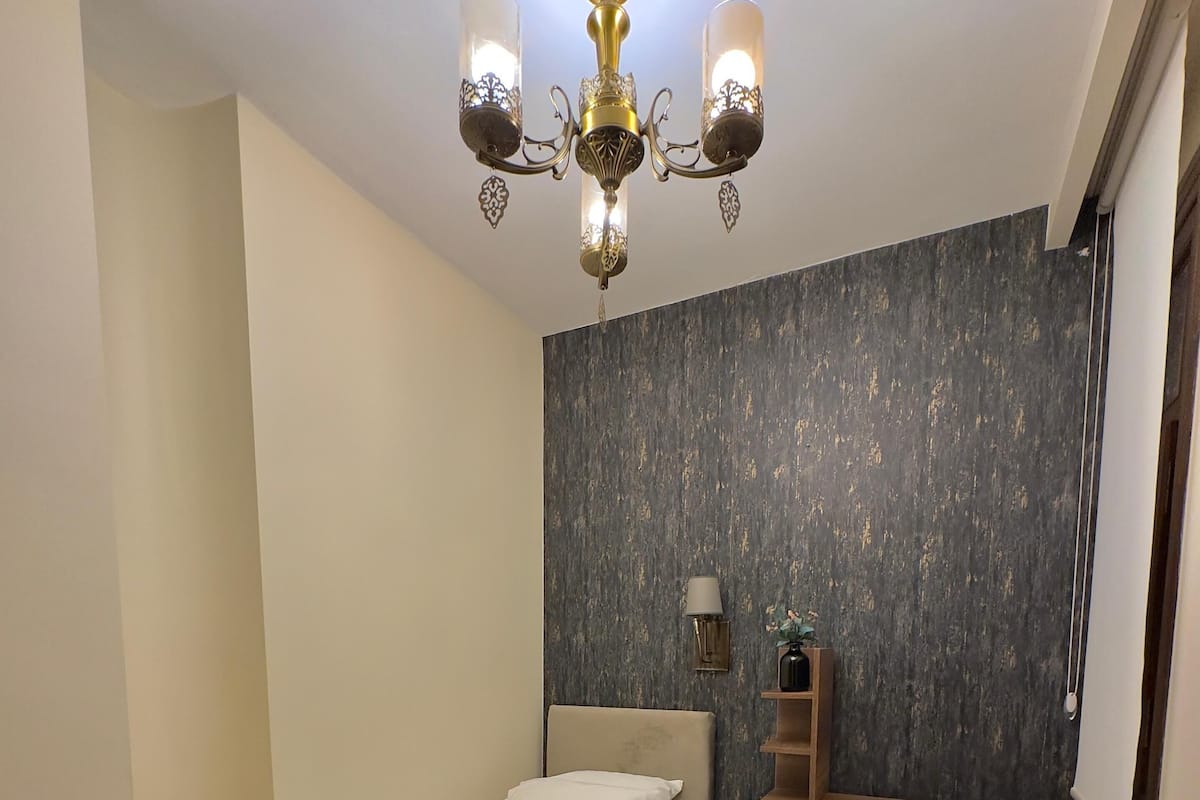 Une chambre d’hôtel comprenant un lit, un bureau, une chaise, une lampe et un lustre décoratif.