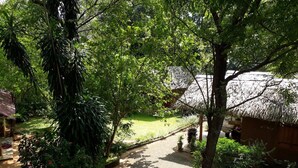 A garden pathway leading to a thatched-roof structure, surrounded by lush greenery and a small seating area.