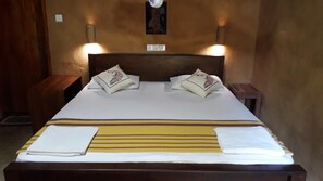 A neatly made bed with pillows, a striped blanket, and two bedside tables with lamps. - Private Organic House (Udawalawa)