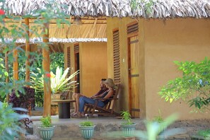 A man and a woman sitting on a wooden bench outside a building with a thatched roof. - Private Organic House (Udawalawa)