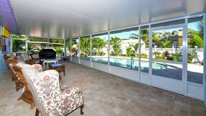 A covered outdoor area with a pool, wicker furniture, and a grill.