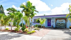 A single-story building with a purple door and windows, surrounded by a variety of tropical plants.