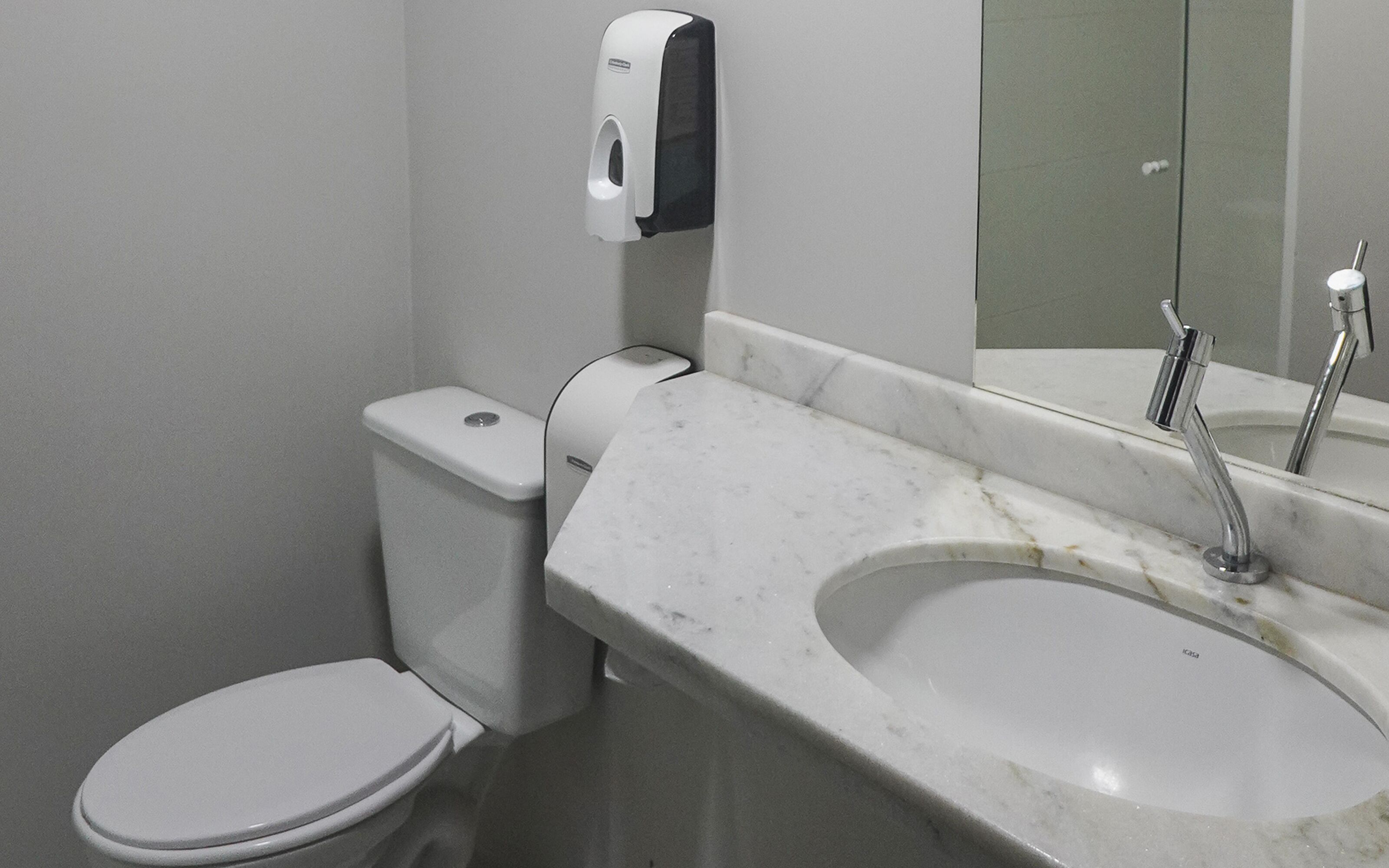 A bathroom with a toilet, a marble sink, and a hand soap dispenser.