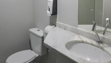 A bathroom with a toilet, a marble sink, and a hand soap dispenser.