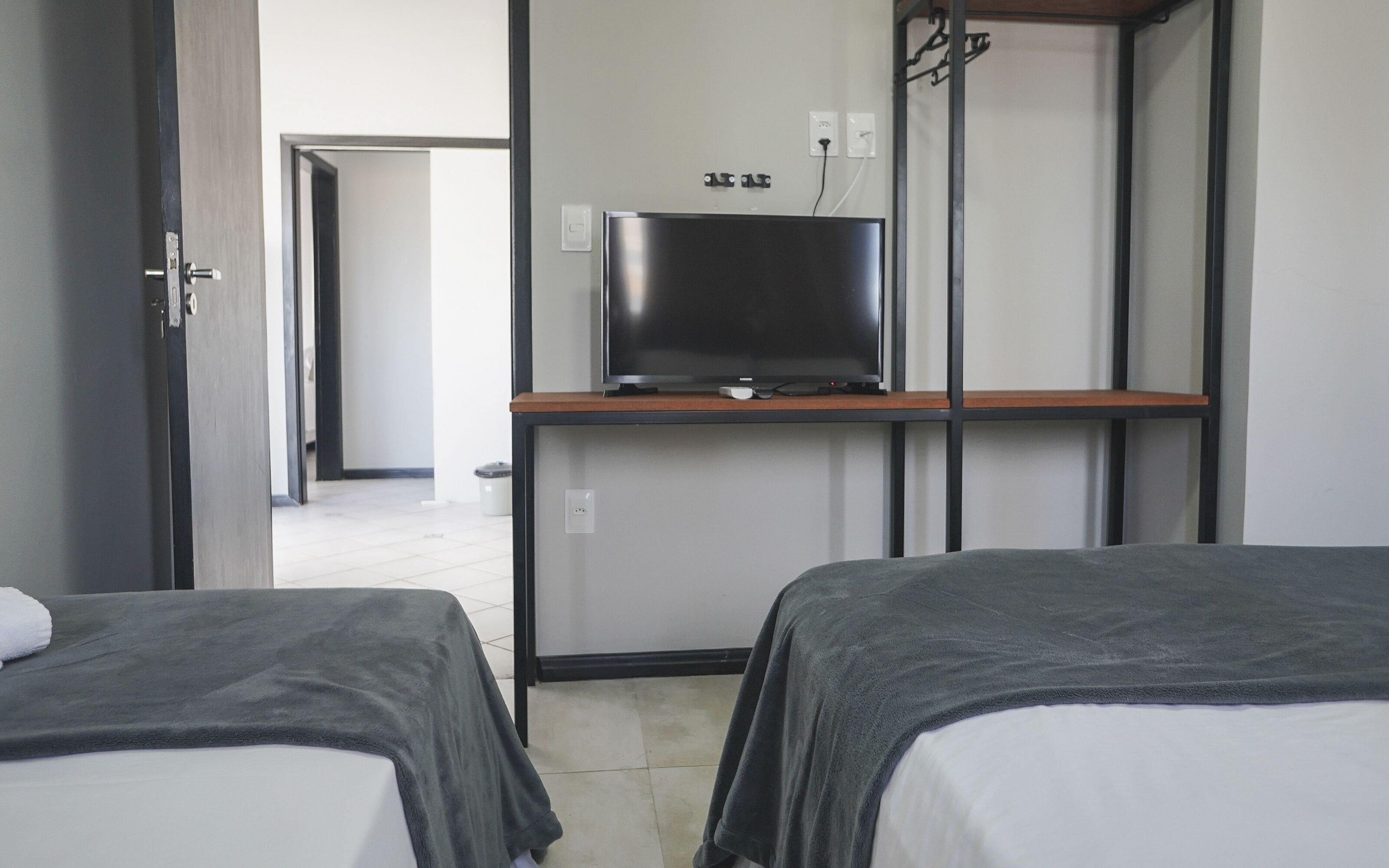 Habitación de hotel con dos camas, un televisor en un estante y una puerta que da a otra habitación.