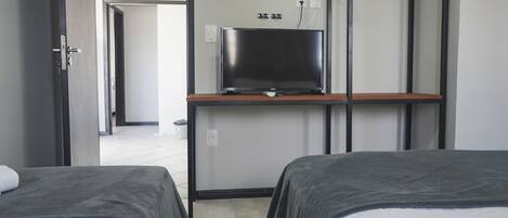 Habitación de hotel con dos camas, un televisor en un estante y una puerta que da a otra habitación.