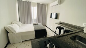 Ein Hotelzimmer mit Bett, Fernseher, einer kleinen Küchenzeile und einem Fenster mit Vorhängen.