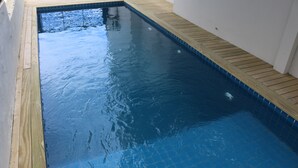 Ein rechteckiger Swimmingpool mit Fliesenboden und einer ihn umgebenden Holzterrasse.