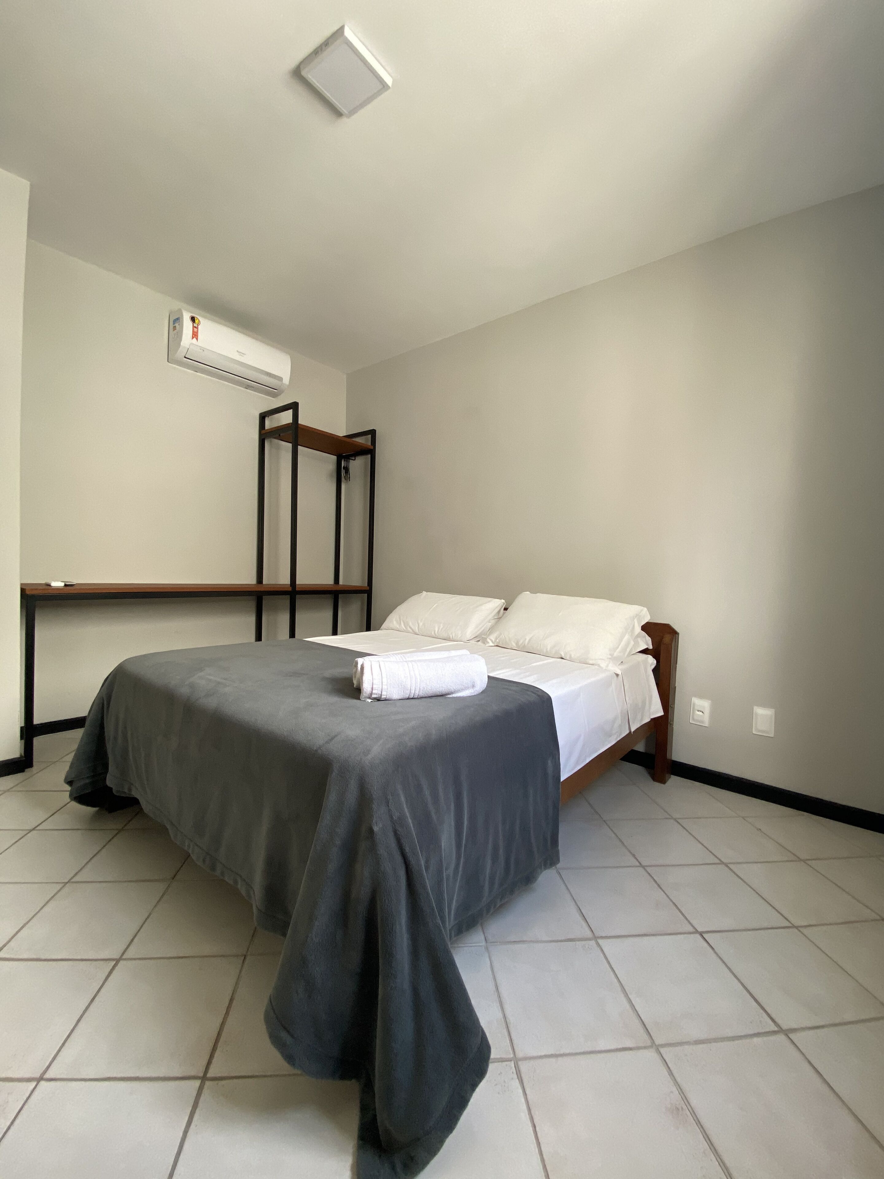 Un dormitorio con cama, mesita de noche, aire acondicionado instalado en la pared y luz de techo.