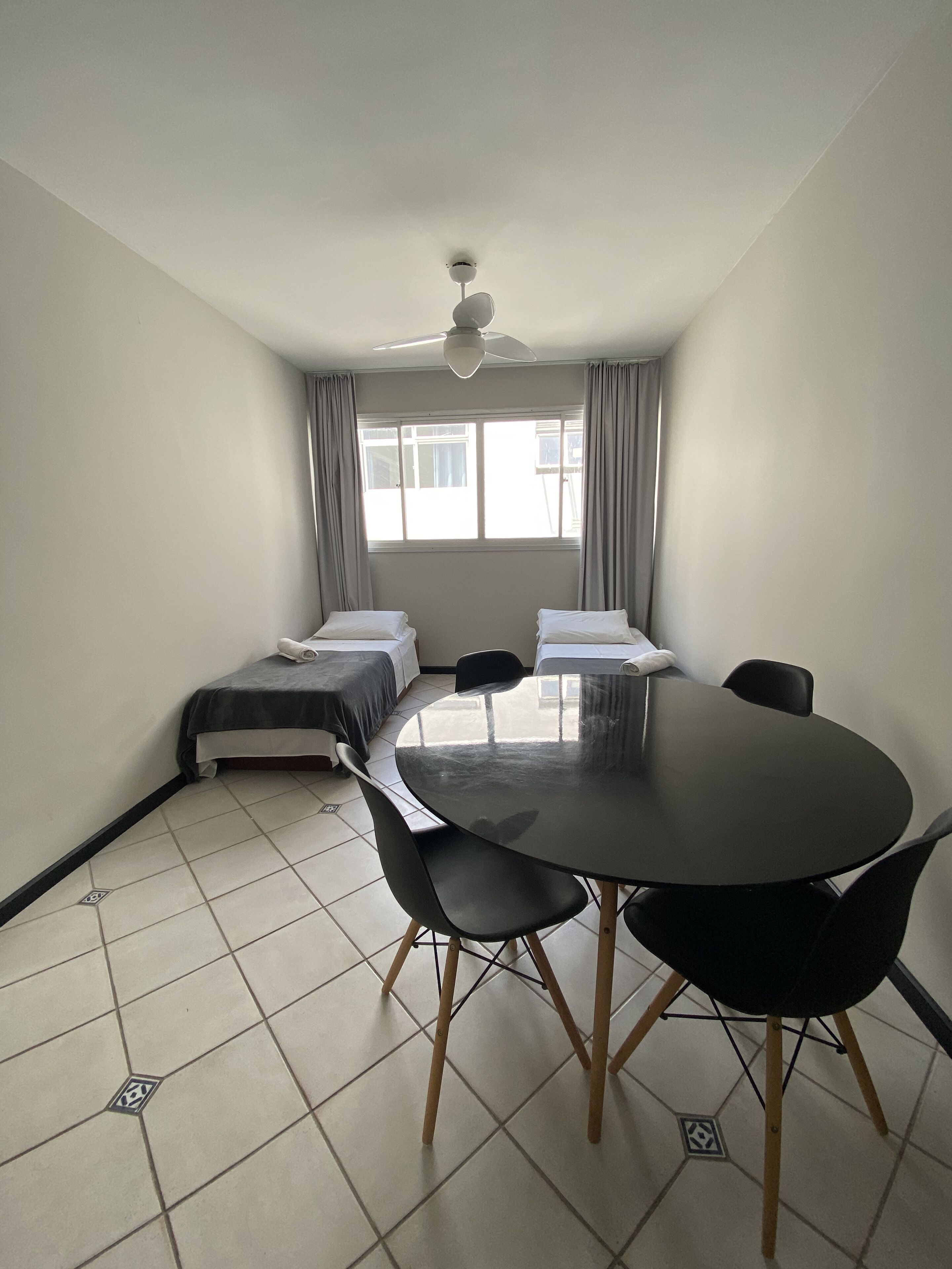 A small, clean room with a round table, two single beds, and a ceiling fan.