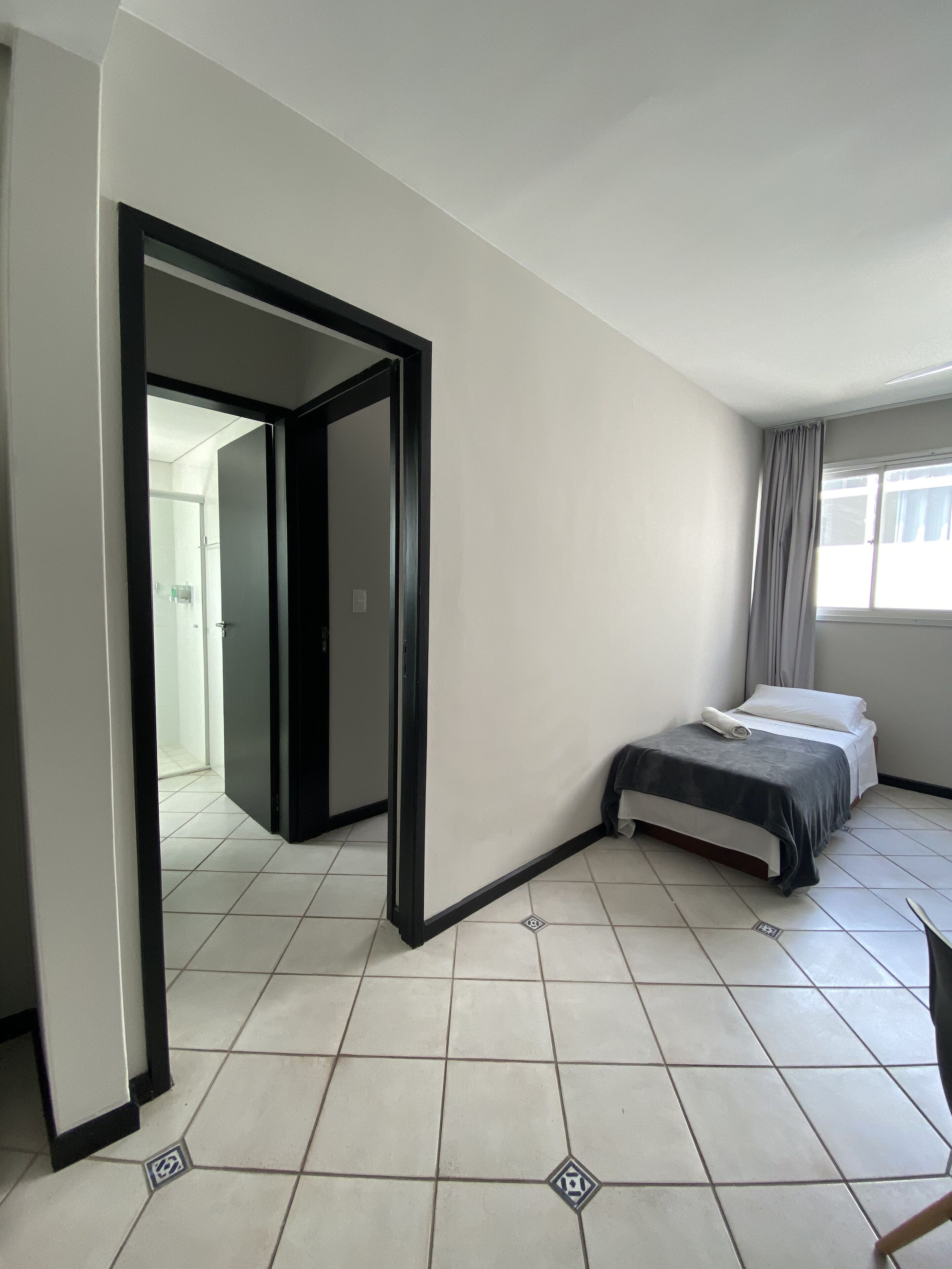 Une chambre d’hôtel avec un lit, une salle de bain visible à travers une porte ouverte et une fenêtre avec des rideaux.