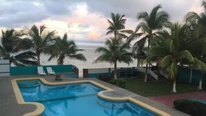 En pool med en unik form, omgivet af palmer og udsigt over havet.