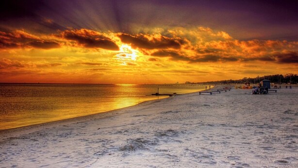 Een strand met een zonsondergang, een pier en enkele mensen.