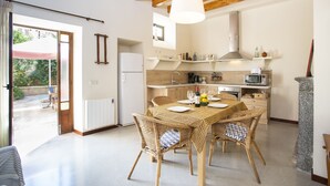 A modern kitchen with a dining area, featuring a table set for four, a refrigerator, and a hanging light fixture. - Ca Sa Padrina. Tradition and charm in Mallorca (Artá)