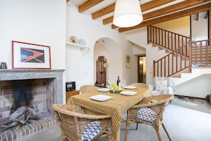 A dining area with a brick fireplace, wicker chairs, a table set for four, and a wooden staircase. - Ca Sa Padrina. Tradition and charm in Mallorca (Artá)