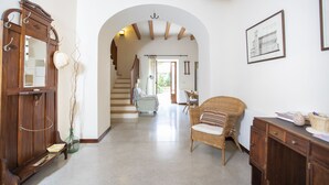 A spacious hallway with a wooden door, a wicker chair, and a framed picture on the wall. - Ca Sa Padrina. Tradition and charm in Mallorca (Artá)