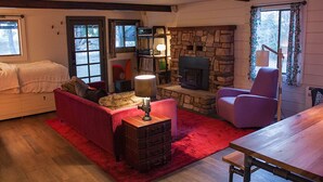A cozy living room with a fireplace, a red sofa, a wooden table, and a stone wall. - Modern and rustic cabin in a beautiful secluded setting (Idyllwild-Pine Cove)