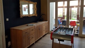 Ett rum med ett träskåp, en spegel, ett fotbollsspel och utsikt över en uteplats med stolar och ett bord.