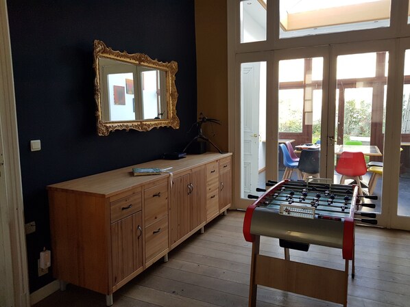 A room with a wooden cabinet, a mirror, a foosball table, and a view of an outdoor patio with chairs and a table.