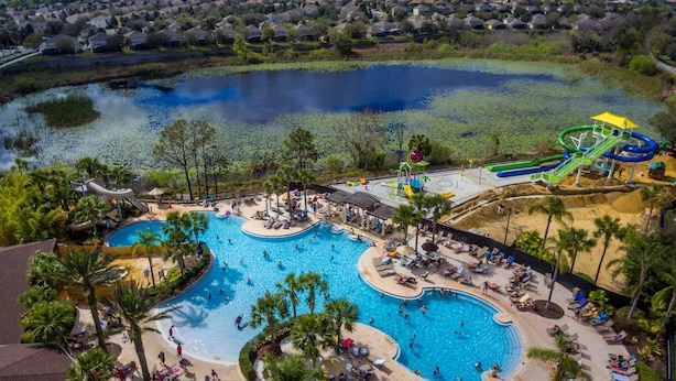 A large outdoor swimming pool with multiple lanes, surrounded by palm trees and a water slide. - Ohana House: 5 Min to WDW! | 100% Renovated | Modern, Luxury, Lakeview, Gameroom (Kissimmee)