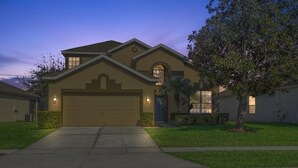 A residential house with a garage, a well-maintained lawn, and a tree. - Ohana House: 5 Min to WDW! | 100% Renovated | Modern, Luxury, Lakeview, Gameroom (Kissimmee)