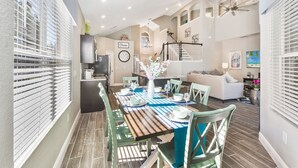 A dining area with a wooden table set for four, surrounded by green chairs, a kitchen in the background, and a staircase leading to an upper level. - Ohana House: 5 Min to WDW! | 100% Renovated | Modern, Luxury, Lakeview, Gameroom (Kissimmee)