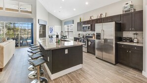 A modern kitchen with dark cabinetry, stainless steel appliances, and a central island with bar stools. - Ohana House: 5 Min to WDW! | 100% Renovated | Modern, Luxury, Lakeview, Gameroom (Kissimmee)