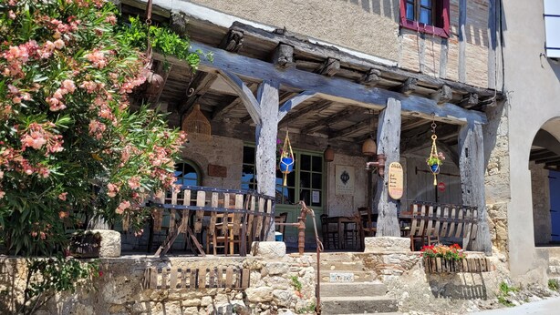 Un bâtiment rustique en pierre, doté d’un porche en bois, d’escaliers en pierre et de décorations suspendues.