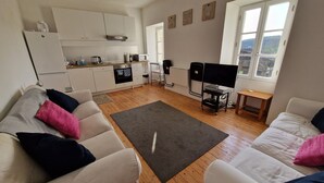 Un salon moderne avec un canapé, une table basse et un téléviseur. Il y a également un coin cuisine équipé de placards et d’appareils électroménagers.